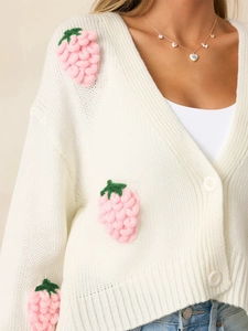 Détail de fraises 3D au crochet sur un cardigan en maille blanc crème à col en V