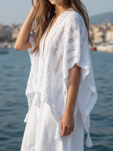 Detail of white crochet knit poncho featuring bohemian hollow patterns and tassel fringe