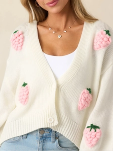 Détail d'appliqués fraises roses en 3D sur un cardigan en maille blanche à col en V