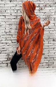 Detail of orange knit hooded poncho featuring colorful stripes and fringe hem