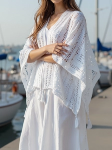 Close-up of white crochet shawl featuring intricate hollow lace and bohemian tassel hem
