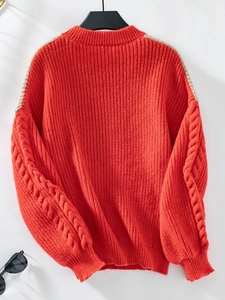 Detail eines roten Zopfstrickpullovers mit vertikalem Rippmuster und beiger Kontrastnaht