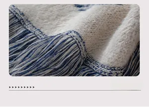 Close-up of cream knit fabric with blue jacquard patterns and woven tassel fringe detail