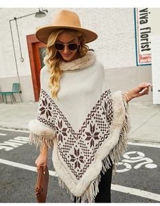 Detail of white knit poncho featuring snowflake patterns, faux fur collar, and fringe hem