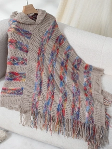 Detail of colorful striped knit poncho with fringe trim and hood on a wooden hanger