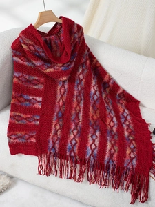 Close-up of red cable-knit poncho with colorful stripes and long fringe detailing