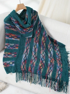 Close-up of thick green knit poncho with colorful geometric patterns and long fringes