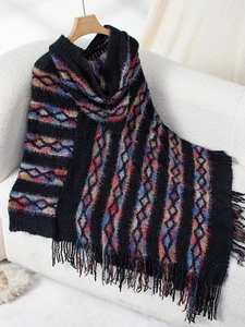 Detailed close-up of knit poncho featuring colorful geometric patterns and black fringes