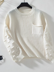 Detail of white knit sweater showing textured puff ball sleeves and chest pocket