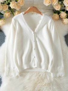 Close-up of white knit cardigan with elegant lace trim and v-neck button details