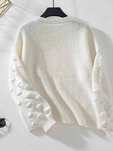 Close-up of white knitted sweater featuring textured 3D pom-pom dots on sleeves