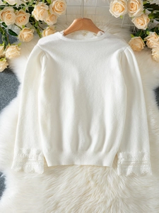 Detail of elegant lace patchwork on V-neck collar and cuffs of white knit cardigan