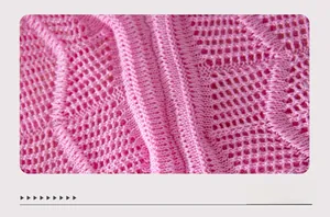 Close-up of pink knit fabric showing detailed hollow crochet pattern and soft texture