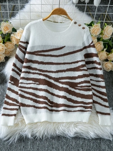 Detail of knit sweater shoulder showing golden buttons and zebra stripe texture