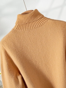 Detailed close-up of camel turtleneck knitwear featuring a refined ribbed collar texture