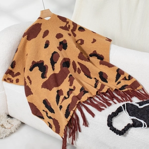 Detail shot of leopard print knit poncho with long brown fringes on a textured sofa