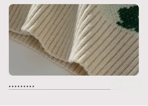 Détail en maille beige douce avec poignets côtelés et motif jacquard trèfle vert