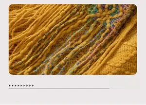 Detailed close-up of yellow knit shawl hem with fringe and colorful braided accents