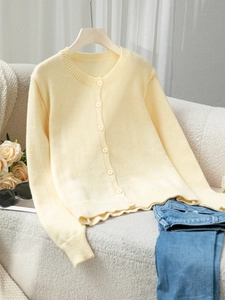 Close-up of a soft pale yellow knit cardigan with buttons and ribbed texture on a sofa