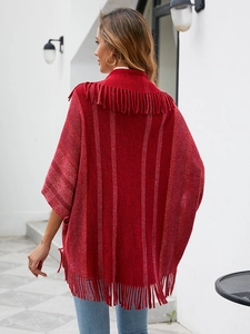 Gros plan d'un poncho en tricot rouge doux avec des franges et des rayures verticales