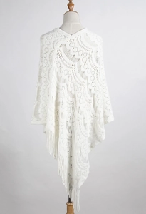 Detail of white crochet hollow-out knit shawl with intricate wave patterns and long tassels