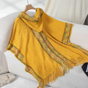 Detail of yellow knit poncho featuring diamond textures and ethnic tassel trim