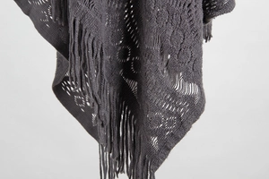 Detail of dark grey knit poncho showing hollow crochet patterns and long fringe tassels