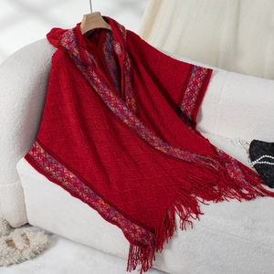 Close-up of red knitted poncho with ethnic trim, diamond texture and long fringe detail