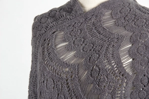 Close-up of dark grey crochet hollow-out pattern and fringe on women's knit shawl poncho