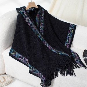 Detail of ethnic knit poncho featuring colorful patterned trim and black fringe tassels