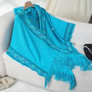 Detail of teal knit poncho featuring ethnic embroidery borders and soft fringe trim