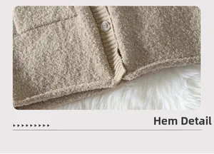 Macro detail of beige knit cardigan fabric showing amber button and ribbed hem texture