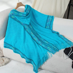 Detail of blue knitted poncho with ethnic ribbon trim, fringe hem and hood on a sofa