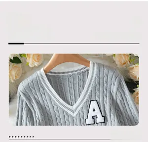 Detailed cable knit texture of light grey V-neck vest featuring a white towel embroidered A