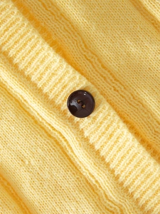 Close-up of bright yellow knit cardigan with vertical texture and stylish brown button
