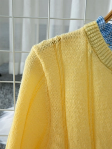 Close-up of soft yellow ribbed knit cardigan with ruffle details and layered plaid collar