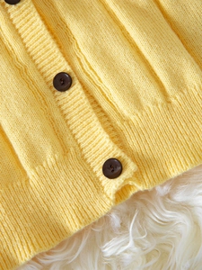 Bright yellow knit cardigan with ruffled edges and brown buttons on white plush background