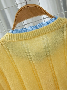 Detailed view of yellow ribbed knit fabric with blue plaid collar and wooden hanger