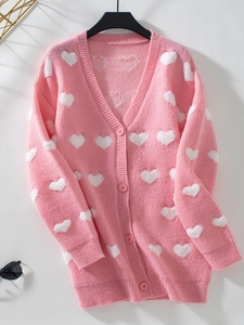 Détail d'un cardigan en maille rose avec motifs cœurs blancs et boutons assortis