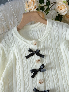 Détail macro de maille torsadée et nœuds en satin noir sur cardigan en tricot ivoire