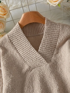 Détail du col en V nervuré d'un pull en maille abricot sur un cintre en bois