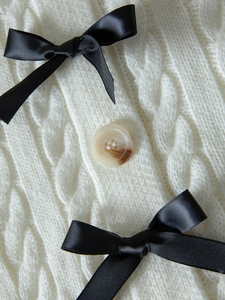 Détail macro de maille torsadée crème avec nœuds en satin noir et bouton ambre
