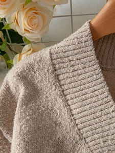 Détail macro du pull en maille beige montrant les poignets côtelés et la texture douce