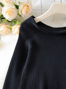 Detailed view of black ribbed knit sweater featuring an elegant boat neck and fine texture