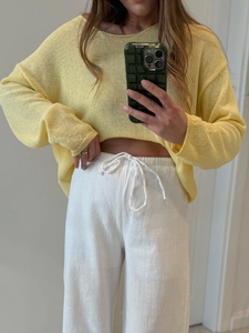 Dettaglio di un maglione giallo chiaro e pantaloni bianchi con coulisse in vita