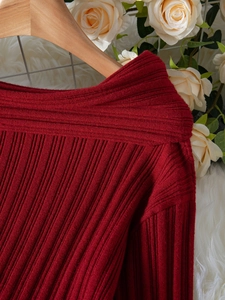 Detail shot of elegant red ribbed knit sweater featuring a wide off-the-shoulder neckline