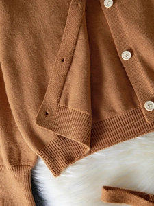 Detail of dark brown knit cardigan featuring white buttons and ribbed texture cuffs