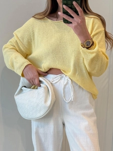 Maglione giallo a maglia traforata abbinato a borsa in pelle intrecciata e pantaloni bianchi