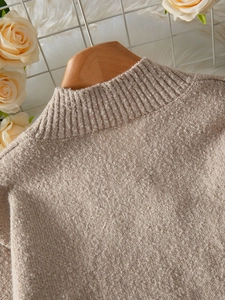 Détail d'un pull en maille beige montrant le col rond côtelé sur un cintre