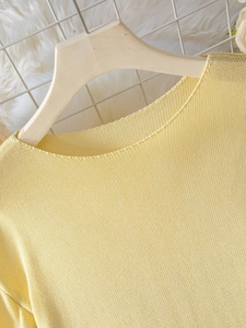 Dettaglio del girocollo con bordo arrotolato su un maglione giallo da donna